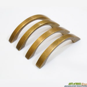 May include: Four antique brass cabinet door pulls with a curved design. The pulls are arranged in a staggered pattern.