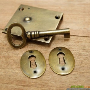May include: Antique brass keyhole escutcheon set with a key. The escutcheons are oval shaped with a keyhole in the center. The key is ornate with a heart-shaped hole in the bow.