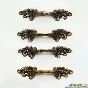 May include: Four antique brass drawer pulls with ornate floral designs. Each pull has a curved shape and a smooth, polished finish.