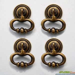 May include: Four antique brass cabinet door pulls with a ring handle and a round base. The pulls have a distressed finish and are in excellent condition.