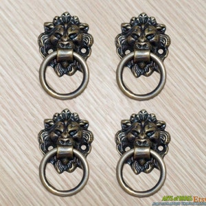 May include: Set of four antique brass lion head drawer pulls with ring handles. Each pull features a detailed lion head with a textured finish.