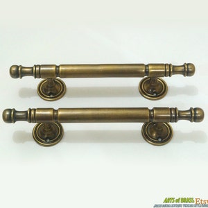 May include: Two antique brass door handles with a simple, elegant design. Each handle features a round, decorative base and a long, straight bar with a rounded end.