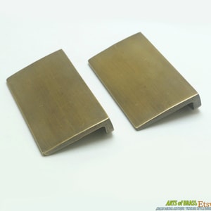 Könnte beinhalten: Zwei antike Messing-Schrankgriffe mit abgeschrägter Kante. Die Griffe sind rechteckig und haben eine gebürstete Oberfläche.