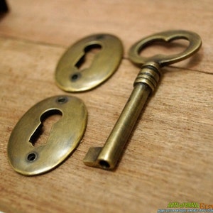 May include: Two oval brass keyhole covers and a brass skeleton key with a heart-shaped keyhole. The keyhole covers have a worn, antique finish.