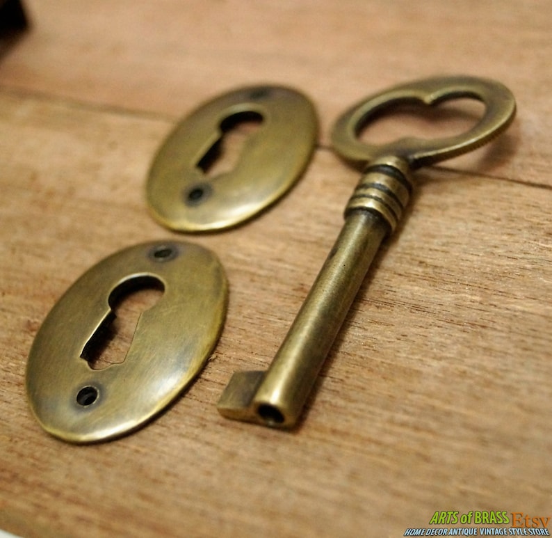 May include: Two oval brass keyhole covers and a brass skeleton key with a heart-shaped keyhole. The keyhole covers have a worn, antique finish.