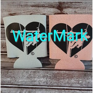 May include: Two insulated beverage holders with a black heart design featuring a silhouette of a person climbing a utility pole. One holder is light blue and the other is pink.