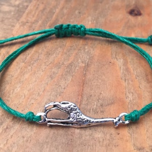Puede incluir: Un brazalete de cuerda verde con un dije de plata en forma de garra de dinosaurio.
