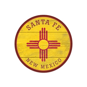 May include: A round wooden sign with a yellow background and a red border. The sign features the state of New Mexico's symbol, a red Zia sun symbol, and the text "SANTA FE NEW MEXICO".