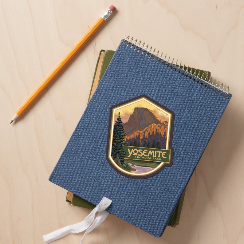 Puede incluir: Una libreta azul con espiral y una pegatina con una ilustraci&oacute;n de estilo vintage del Parque Nacional de Yosemite. La pegatina tiene un borde dorado y el texto "Yosemite National Park".