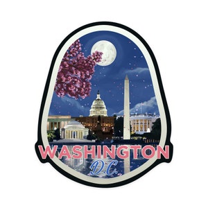 May include: A sticker featuring a nighttime view of Washington D.C. with the Washington Monument, the Capitol Building, and cherry blossoms in the foreground. The sticker is shaped like a teardrop and has a black outline.