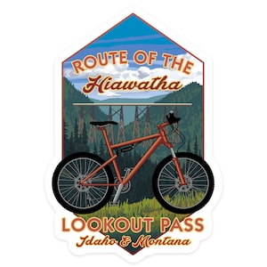 May include: A red mountain bike with a black frame and black wheels is in front of a scenic view of a bridge and forest. The text "ROUTE OF THE Hiawatha LOOKOUT PASS Idaho & Montana" is on the sticker.