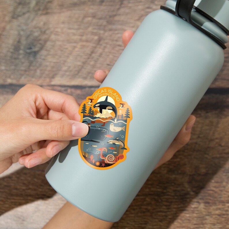 May include: A sticker featuring an illustration of a colorful underwater scene with an orca, a seal, a whale, and various fish. The sticker is on a blue water bottle and says "Orcas Island, Washington State".
