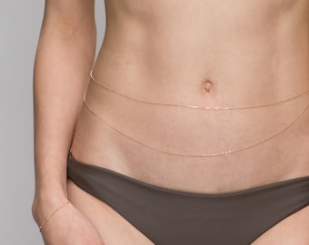 May include: A gold body chain with three strands, worn around the waist.