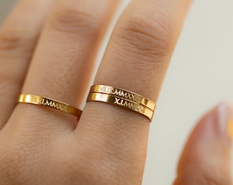 May include: Three gold rings stacked on a finger. The rings are engraved with Roman numerals: VIII.MMXXI, XI.MMXXI, and III.MMXXI.