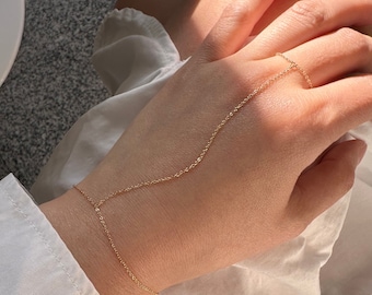 May include: A gold chain bracelet with a delicate design. The chain extends from the wrist to the finger, creating a unique and stylish look.