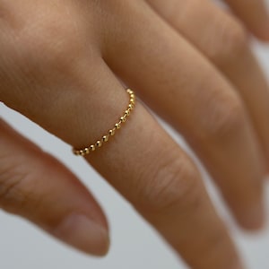 Może przedstawiać: Delikatny złoty pierścionek wykonany z łańcuszka małych, okrągłych koralików.