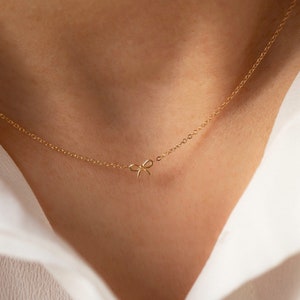 May include: A delicate gold chain necklace with a small bow pendant.