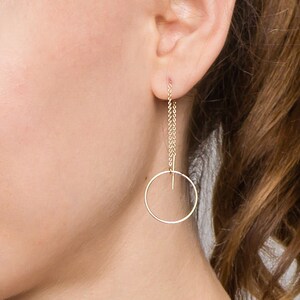 May include: A woman wearing a gold circle dangle earring with a delicate chain.