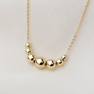 May include: A gold necklace with a chain and a row of graduated round beads.