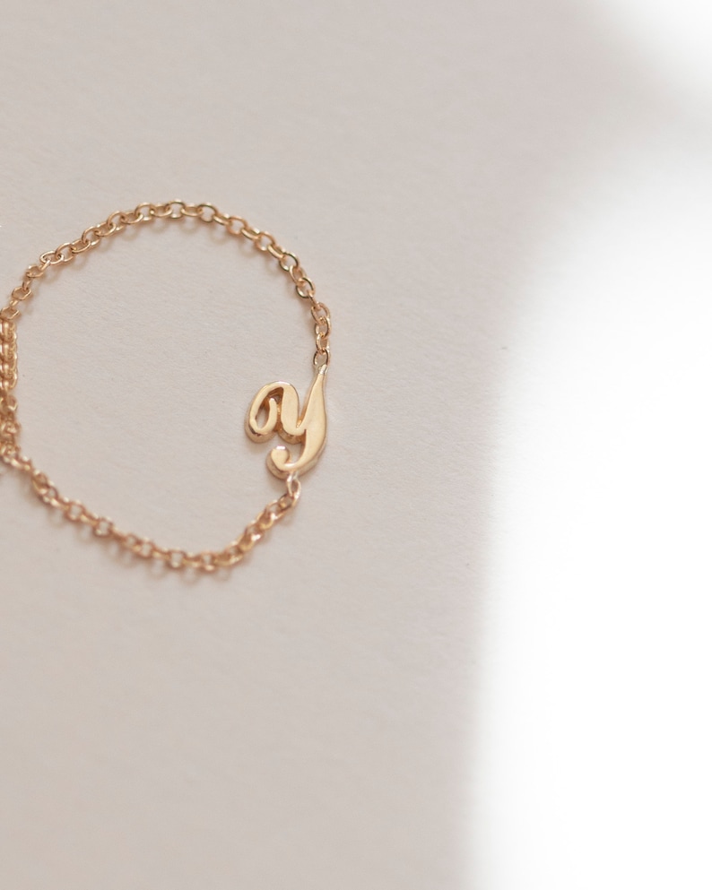 Puede incluir: Un collar de cadena dorada con un colgante de letra 'y' en cursiva.