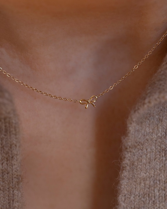 Collana in metallo con ciondolo fiocco e pendaglio perla in plastica
