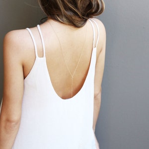 May include: A white tank top with thin straps and a delicate gold chain necklace that hangs down the back.