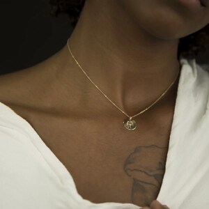 May include: A gold chain necklace with a small round pendant. The pendant has a design of a hand holding a heart.