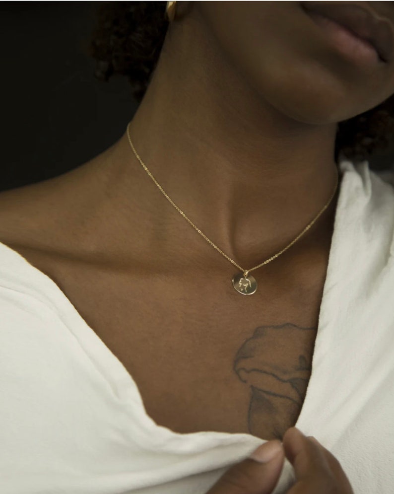 May include: A gold chain necklace with a small round pendant. The pendant has a design of a hand holding a heart.