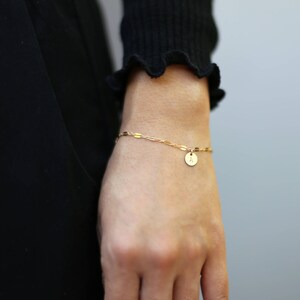 May include: A gold chain bracelet with a small round charm that has the letter 'A' on it.