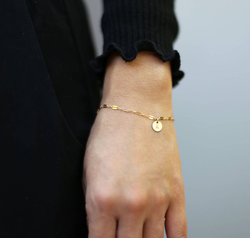 May include: A gold chain bracelet with a small round charm that has the letter 'A' on it.