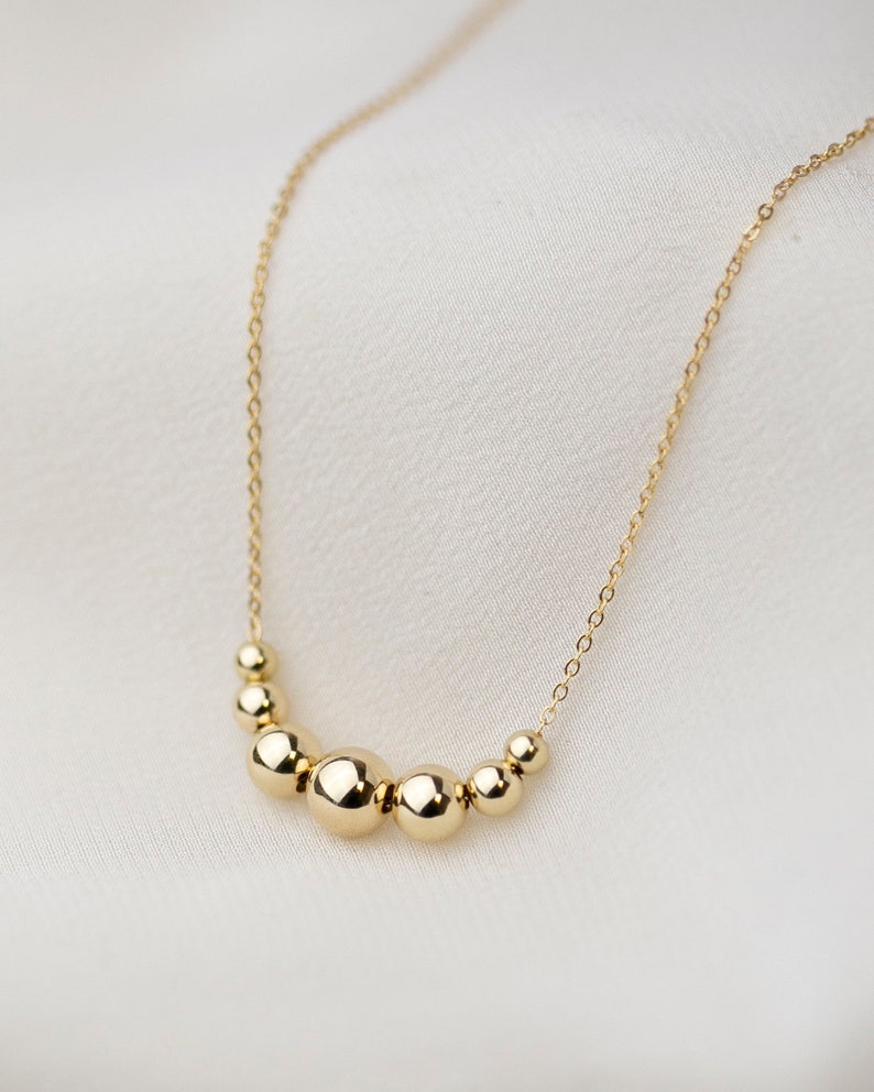 May include: A gold necklace with a chain and a row of graduated round beads.