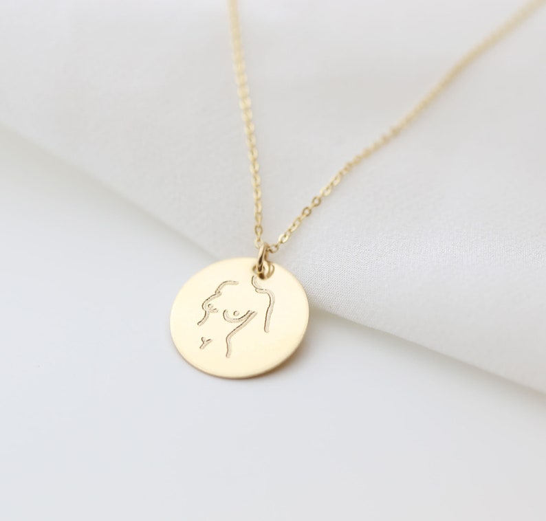 May include: A gold necklace with a round pendant featuring a minimalist line drawing of a female figure.