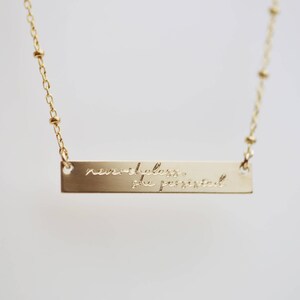 May include: Gold necklace with a bar pendant that reads "nevertheless she persisted".