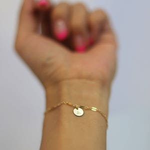 May include: A gold chain bracelet with a small round charm featuring the letter "L".
