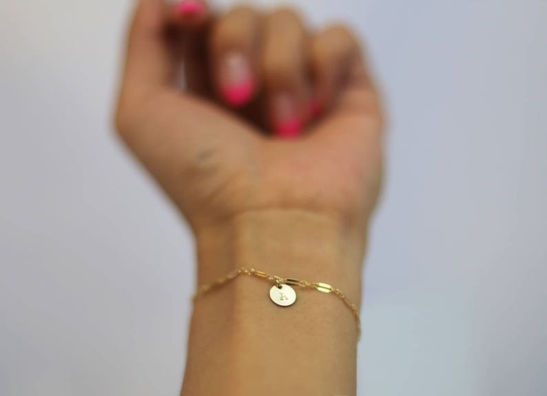 May include: A gold chain bracelet with a small round charm featuring the letter "L".