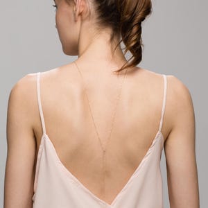 May include: A woman wearing a light pink, sleeveless top with a gold chain necklace that hangs down her back.