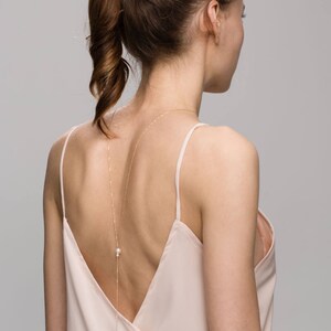 May include: A woman wearing a light pink, sleeveless top with a long, delicate gold chain with pearls hanging down her back.