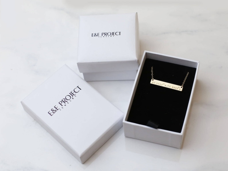 May include: A gold bar necklace with the text "If lost, please return to" on a black velvet background inside a white box with the text "E&E Project Jewelry".