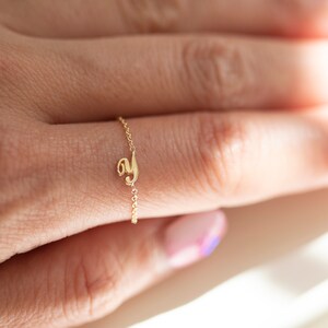 Puede incluir: Un delicado anillo de cadena de oro con un peque&ntilde;o dije con la letra 'y'. El anillo se lleva en un dedo con esmalte de u&ntilde;as rosa claro y azul.