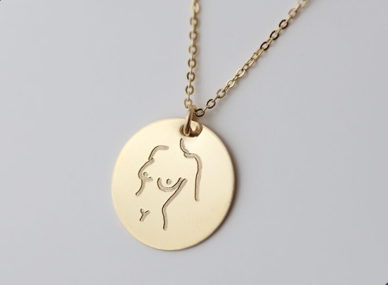 May include: A gold necklace with a round pendant featuring a line drawing of a person's torso.
