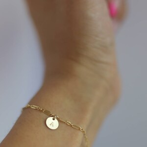 May include: A gold chain bracelet with a small round charm featuring the letter "A".