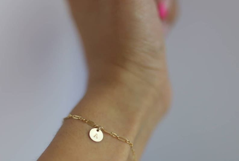 May include: A gold chain bracelet with a small round charm featuring the letter "A".