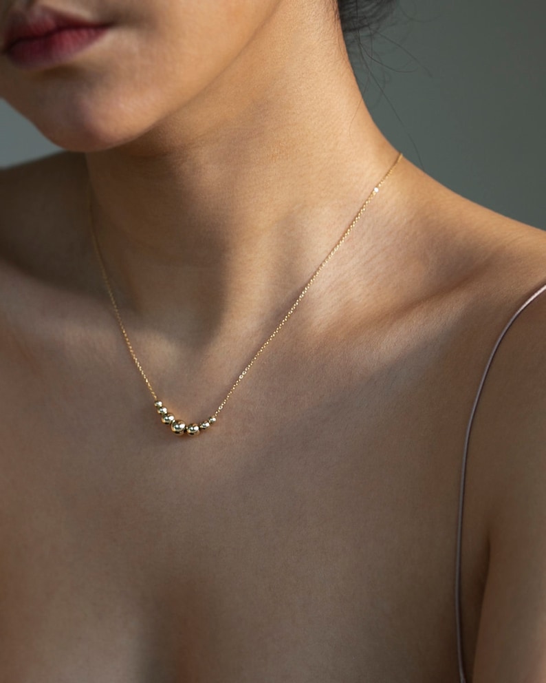 May include: A gold necklace with a curved row of small, round beads.