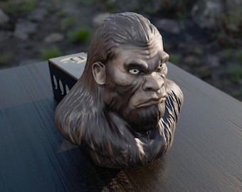 May include: A detailed bust of a Bigfoot-like creature, with a stern expression and dark brown fur. The sculpture sits on a dark wooden surface, with a partially visible box in the background.