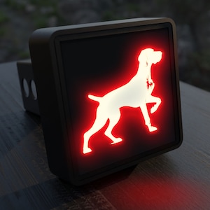 May include: A black metal hitch cover with a red illuminated silhouette of a German Shorthaired Pointer dog.