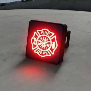 May include: A red and white fire department emblem with the words "FIRE DEPT." inside a black square hitch cover.
