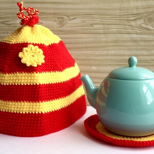 May include: Red and yellow striped crocheted teapot cozy with a yellow flower accent. The cozy is on a white surface next to a light blue teapot on a matching crocheted coaster.