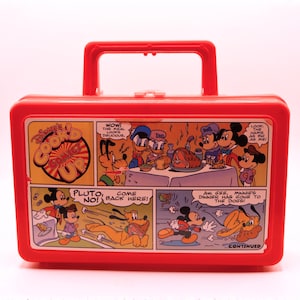 May include: A red plastic lunchbox featuring a comic strip with Disney characters. The lunchbox has a red handle and a graphic of Mickey Mouse, Minnie Mouse, Donald Duck, and Pluto. The text on the lunchbox reads "Disney's Cook Up".