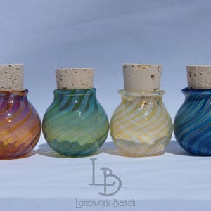 Peut inclure: Quatre petits flacons décoratifs en verre avec des bouchons en liège. Chaque flacon présente une couleur et un motif tourbillonnant uniques : orange, vert, jaune et bleu. Les flacons sont disposés en rangée, mettant en valeur leurs motifs colorés.