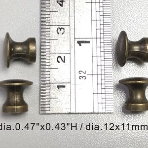 May include: Four antique gold-toned metal knobs with a round top and a cylindrical base. The knobs measure 12mm in diameter and 11mm in height.